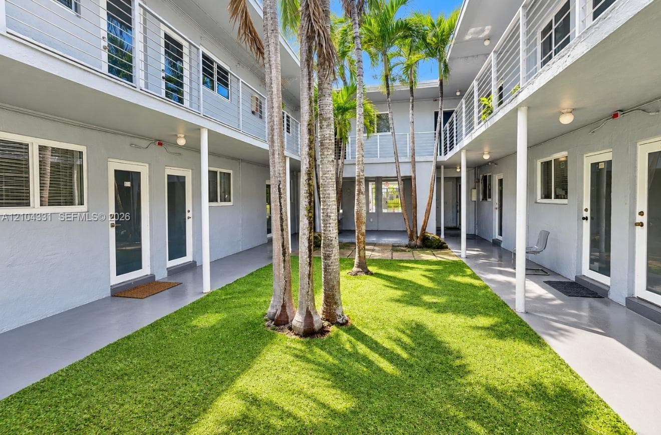 Central courtyard featuring a manicured lawn, established palm trees, two-story covered walkways, and metal cable railings
