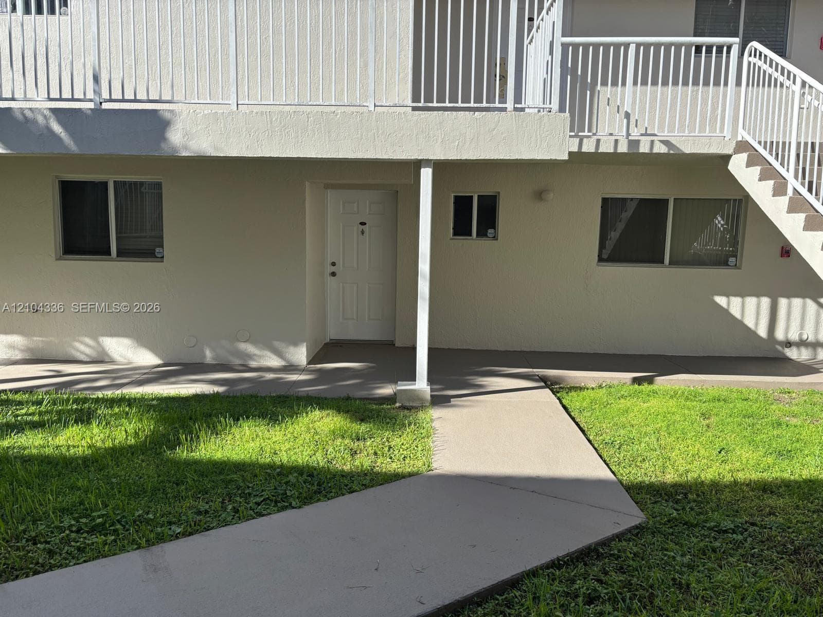 Stucco exterior with sliding windows, covered walkway, concrete pathway, and second-level metal balcony railing