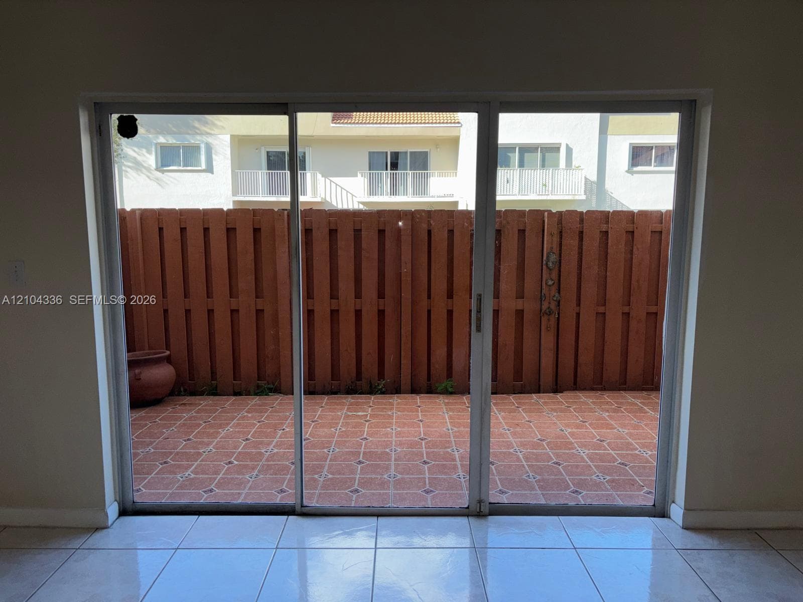 Three-panel sliding glass door opening to a private patio featuring patterned masonry flooring and a vertical wood-plank privacy fence