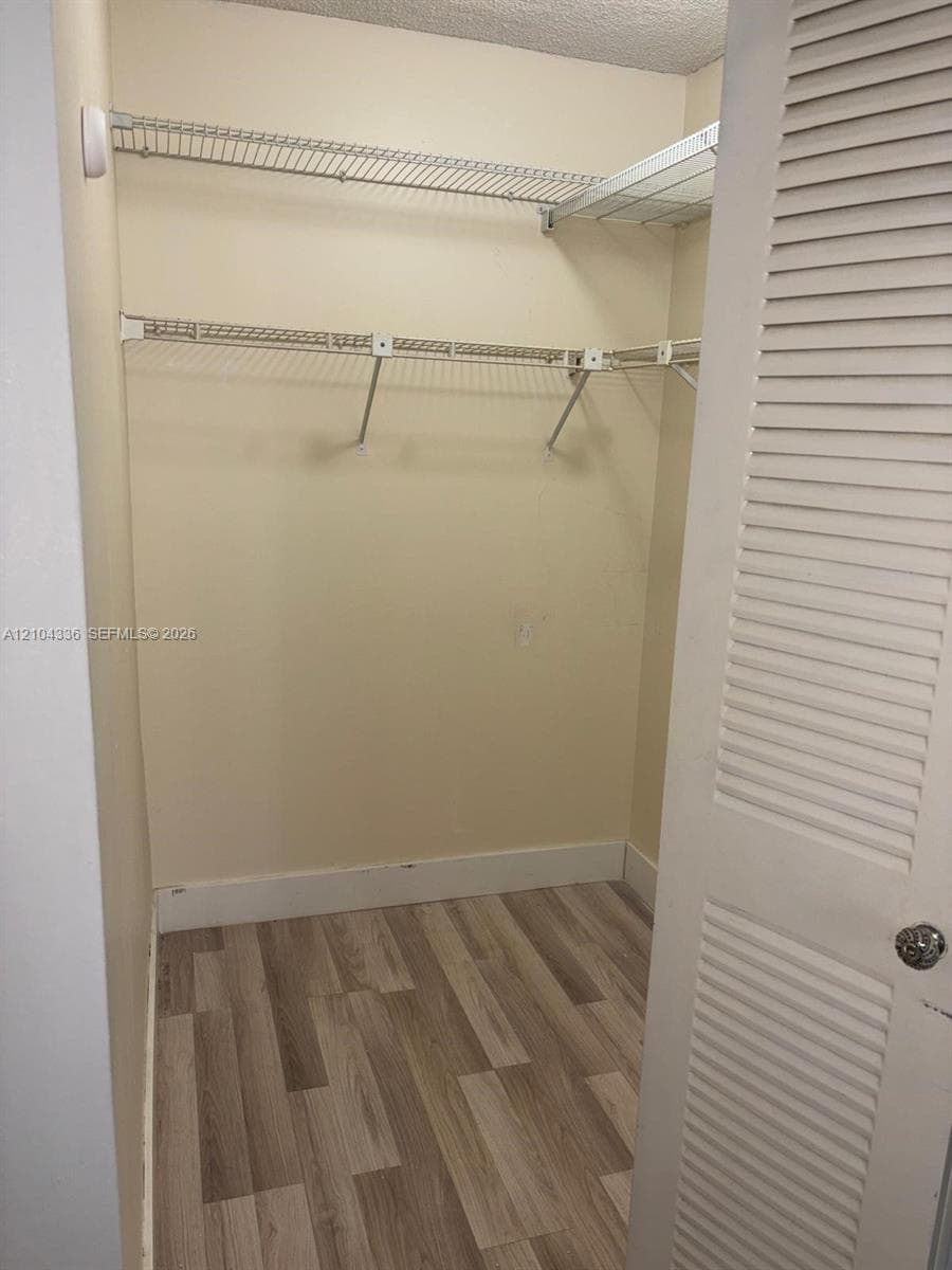 Walk-in storage space featuring wood-finish flooring, multi-level wire shelving, and a louvered bi-fold door