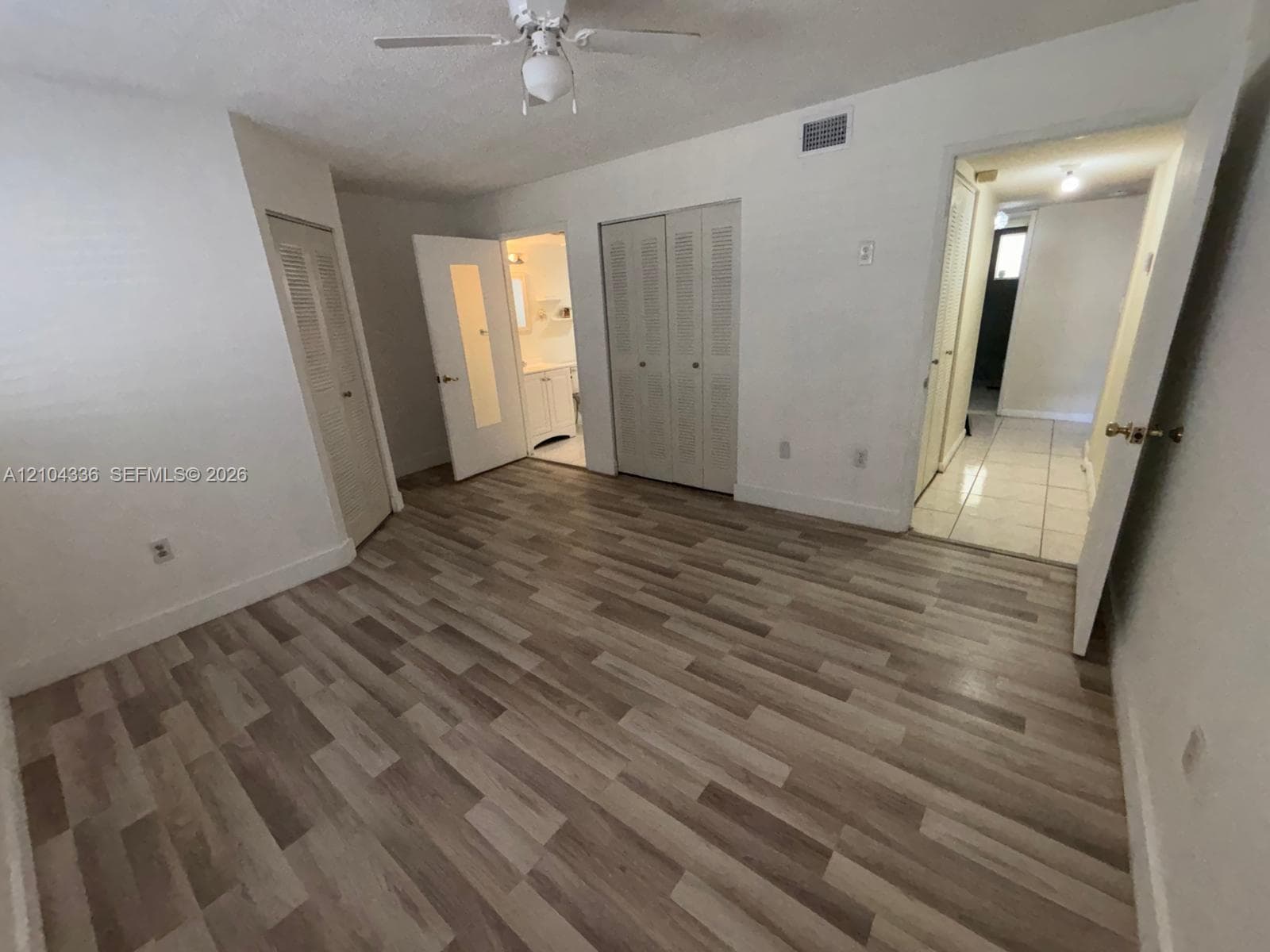 Room featuring wood-finish flooring, a ceiling fan, louvered closet doors, and tile flooring in the entry area