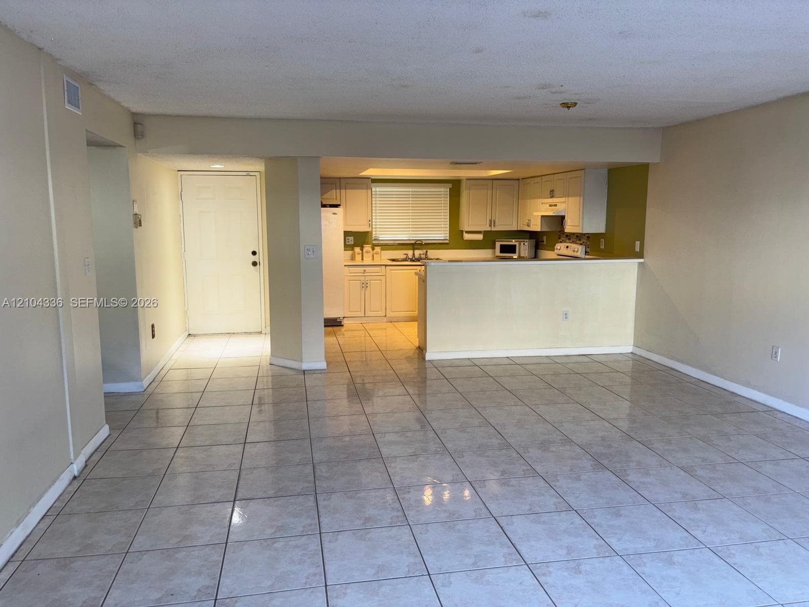 Open-concept interior featuring neutral tile flooring, white cabinetry, a breakfast bar, and window blinds