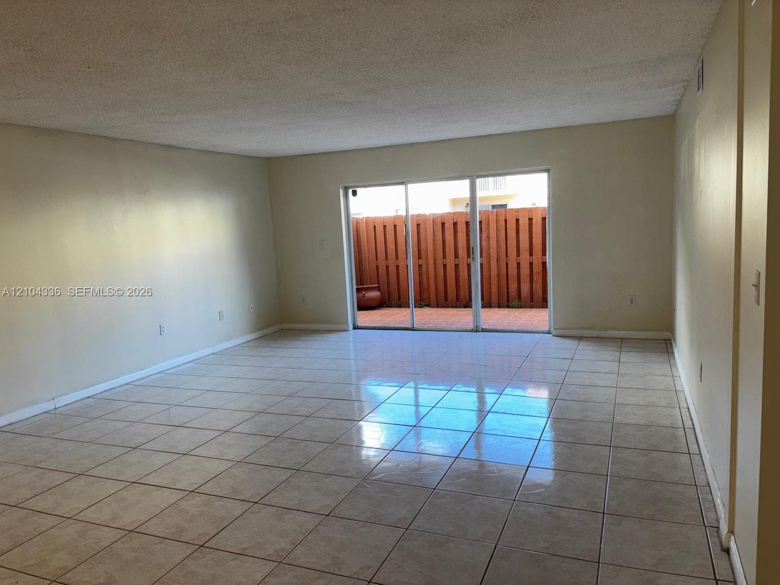 Open-concept room featuring light-toned tile flooring, neutral wall finishes, and expansive sliding glass doors opening to a fenced patio area