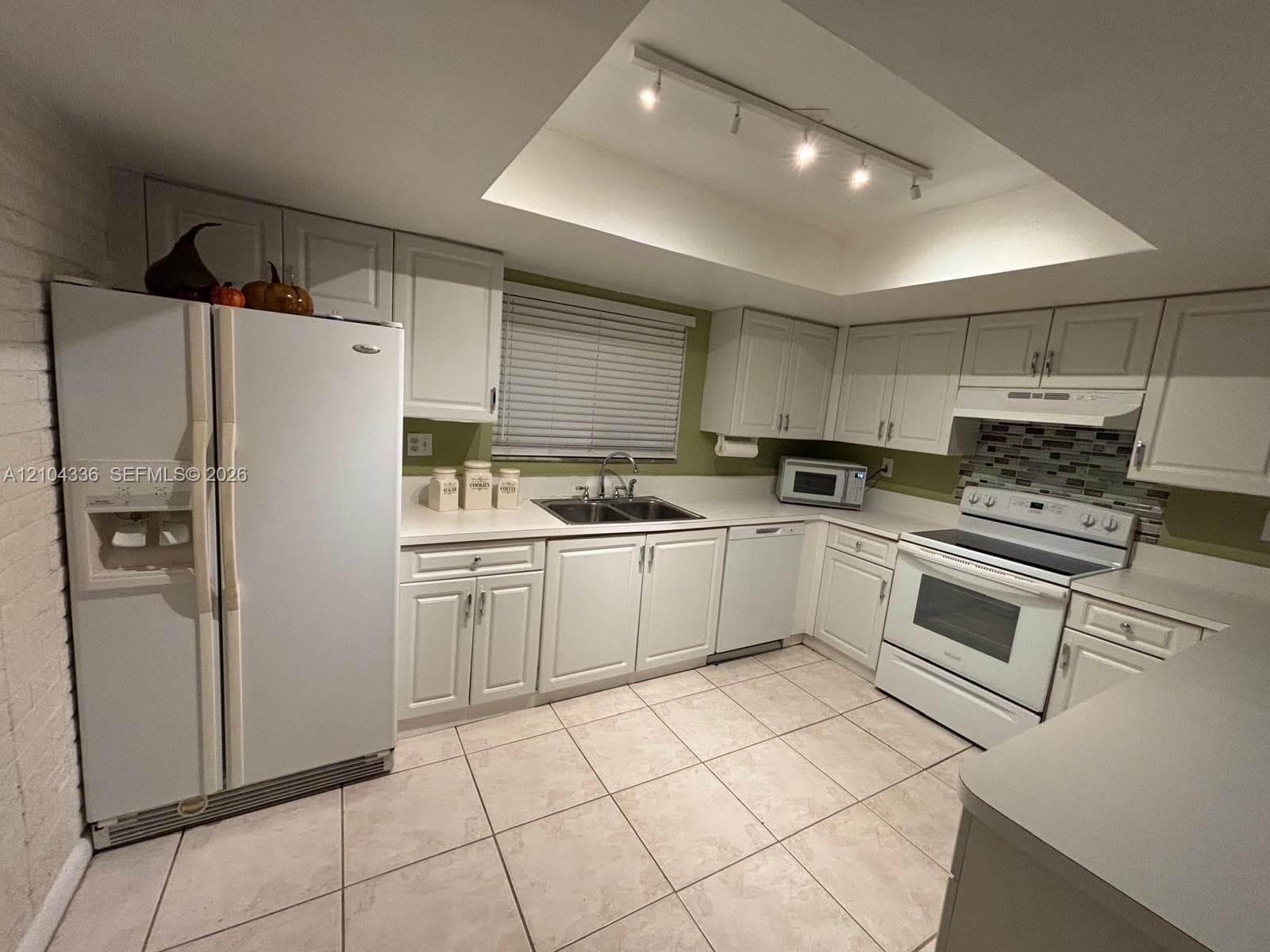 Kitchen featuring white cabinetry, solid surface countertops, tile flooring, built-in track lighting, and a multi-tone tile backsplash