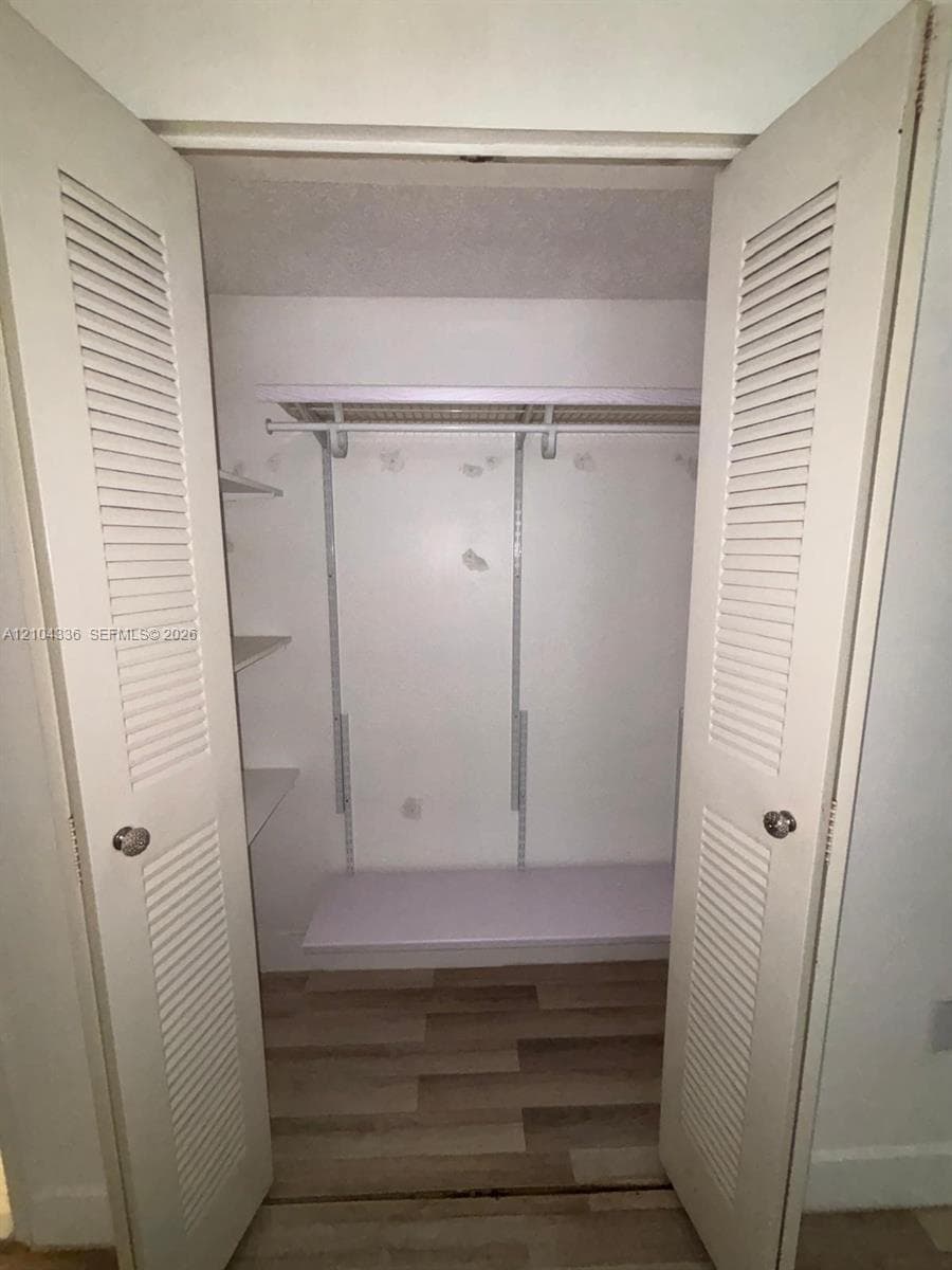 Closet featuring white louvered bifold doors, integrated shelving units, horizontal hanging rods, and wood-finish flooring