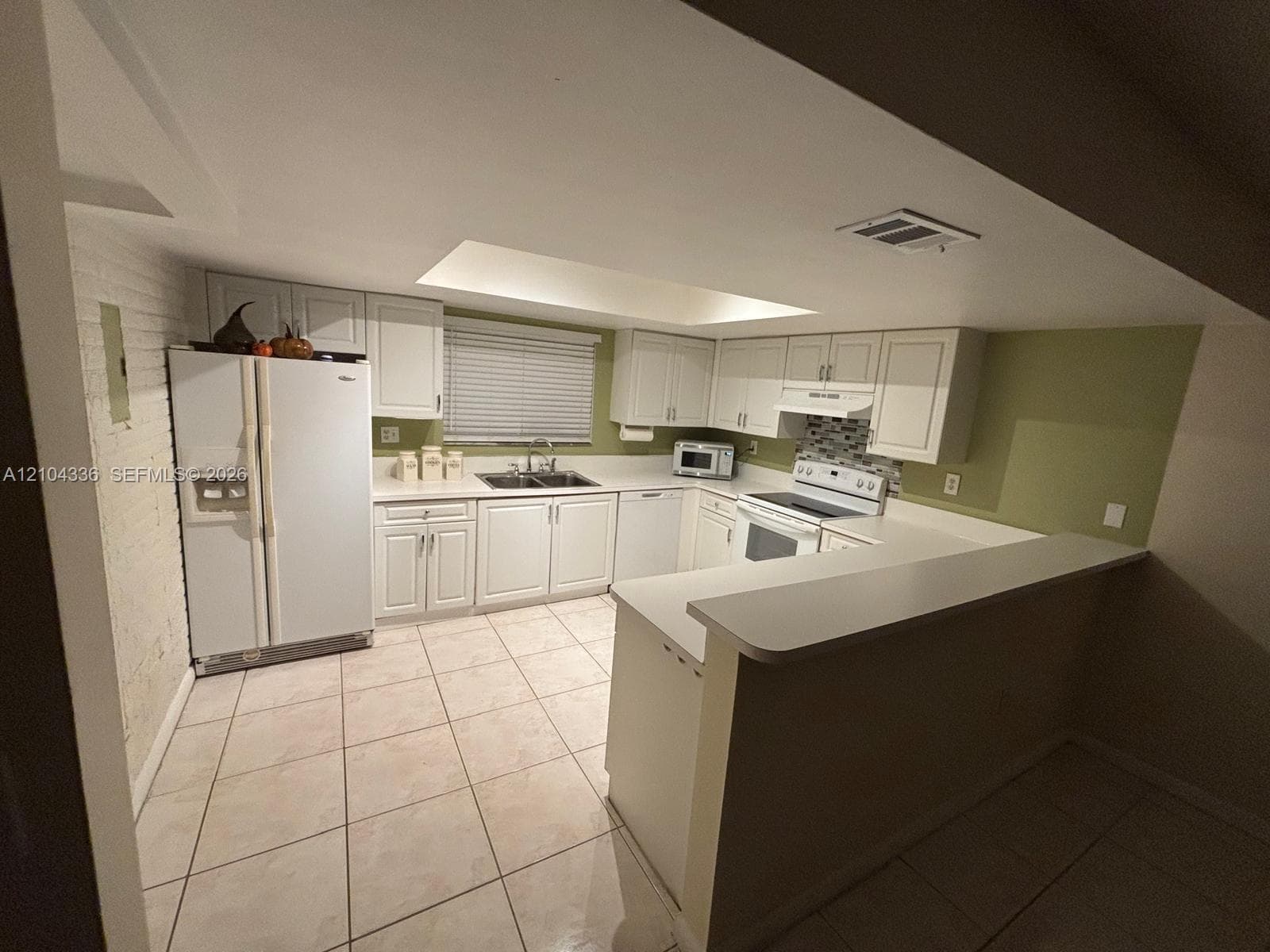 Kitchen featuring white shaker-style cabinetry, tiled flooring, integrated peninsula counter, recessed ceiling lighting, and a brick accent wall