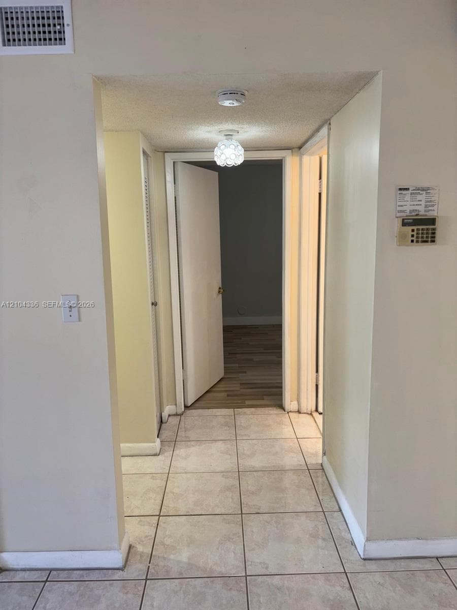 Interior hallway featuring large-format ceramic tile flooring, a multi-faceted spherical pendant light, and doorways with neutral-toned slab doors