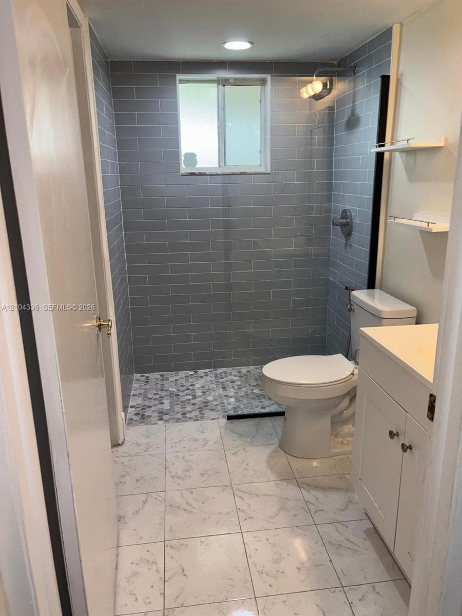 Bathroom featuring large-format tile flooring, gray subway-tiled walk-in shower with a mosaic tile floor, glass shower panel, and built-in shelving