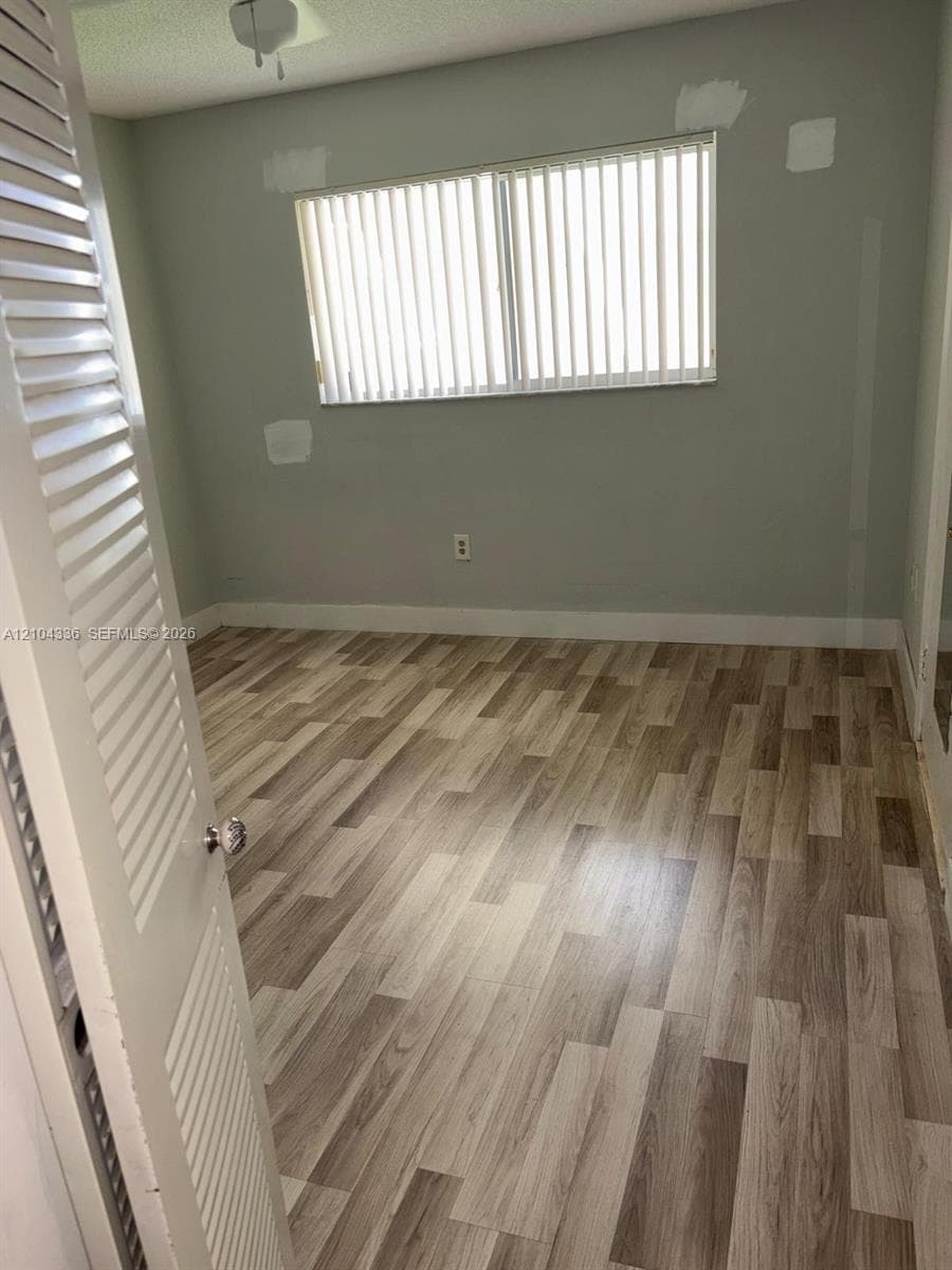 Room featuring wood-finish flooring, a horizontal sliding window with vertical blinds, and a louvered closet door