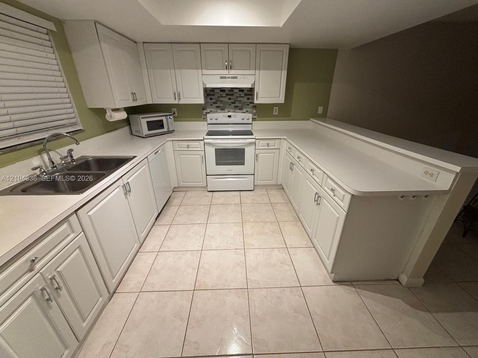 U-shaped kitchen featuring white cabinetry, solid-surface countertops, tile flooring, and a multi-toned mosaic tile backsplash
