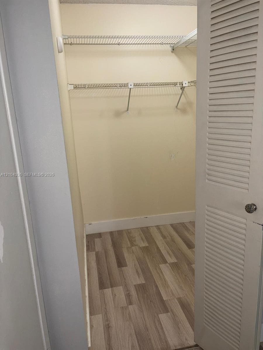 Walk-in closet featuring wood-finish flooring, dual-tier wire shelving, and a louvered door