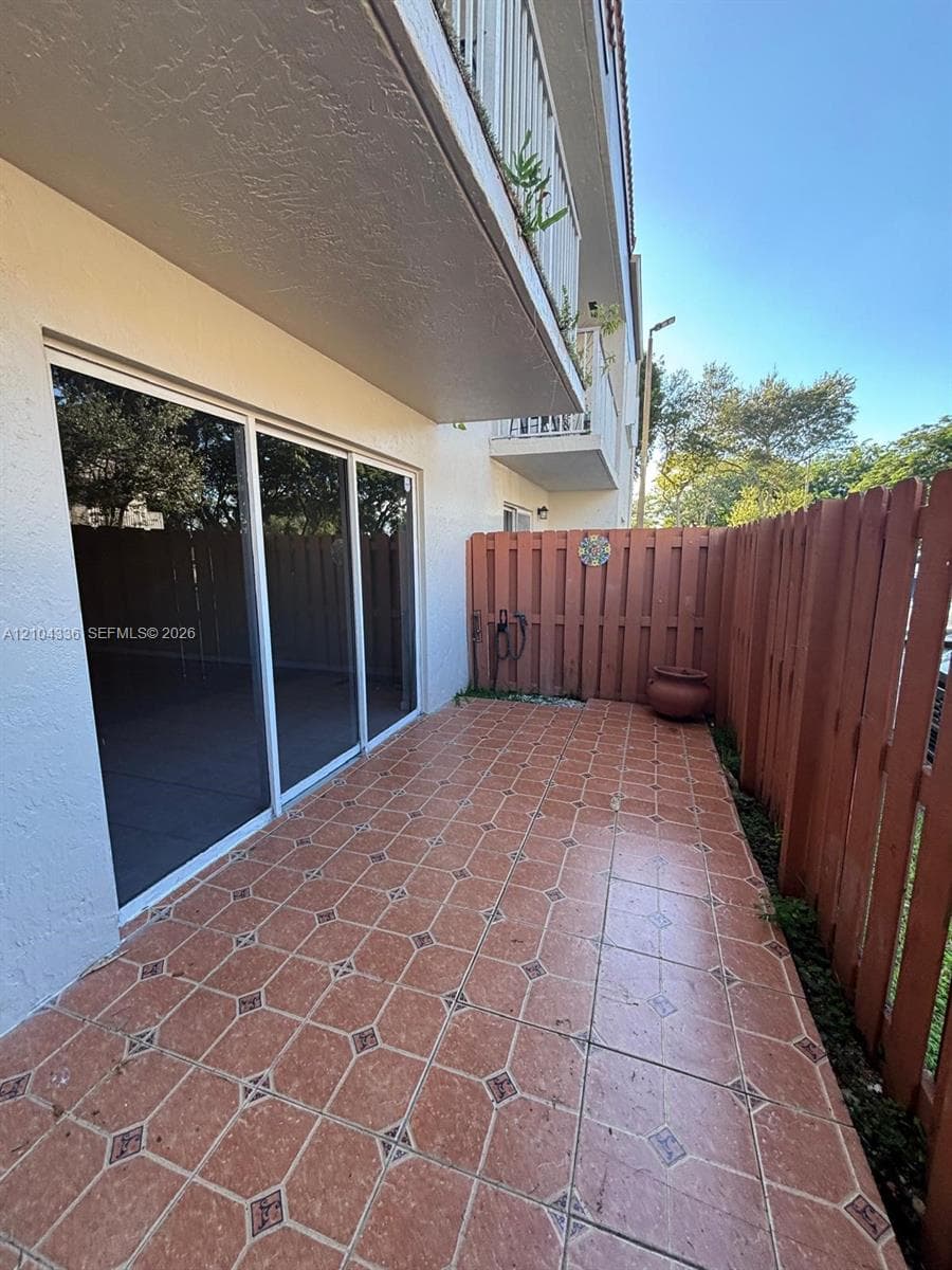 Private patio featuring decorative ceramic tile flooring, a tall wood privacy fence, and a sliding glass door entry