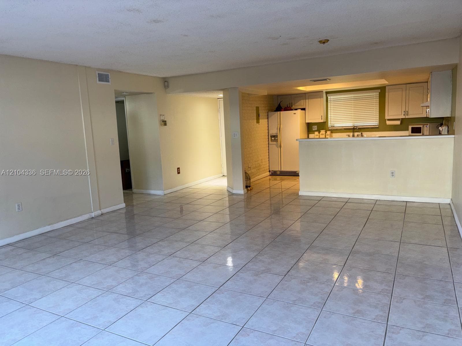 Open-concept interior featuring light-toned tile flooring, a peninsula breakfast bar, white built-in cabinetry, and a brick-finish structural support column