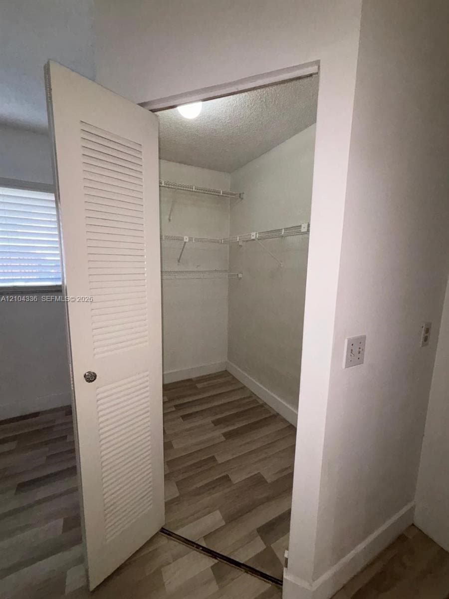Walk-in closet featuring wood-finish flooring, white louvered door, and built-in wire shelving