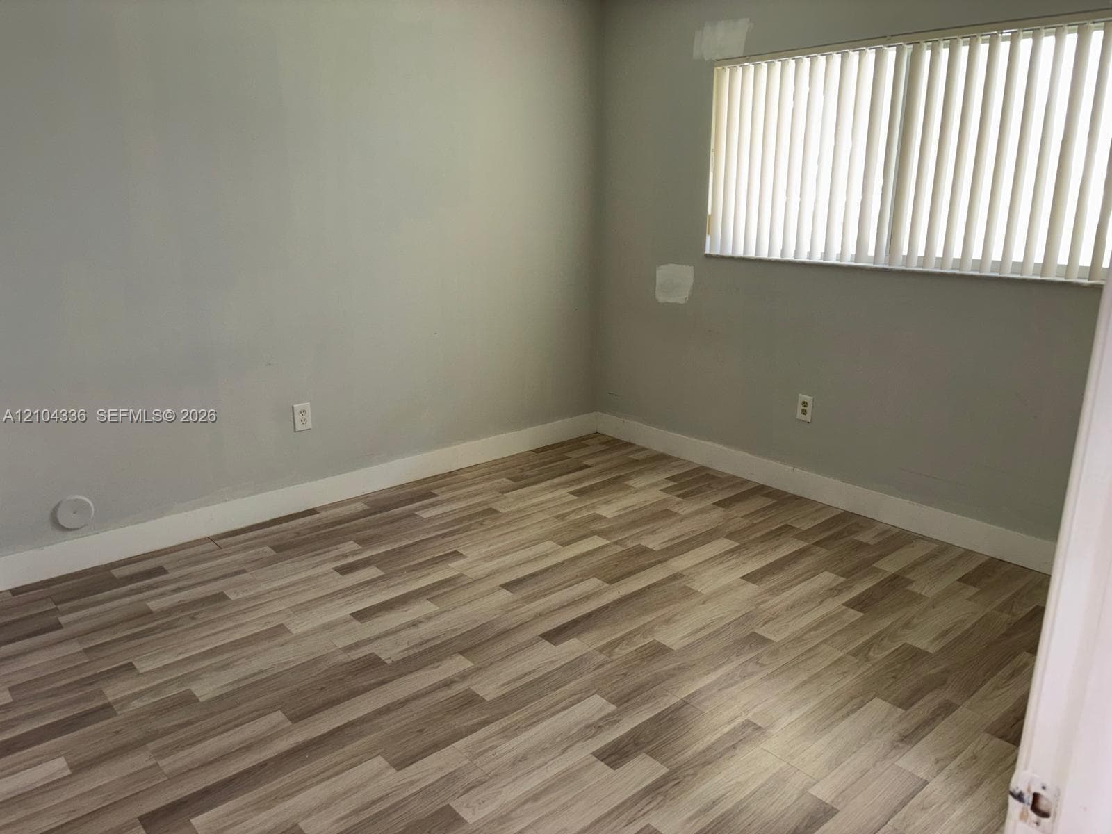 Neutral-toned interior space featuring wood-finish flooring and vertical blinds