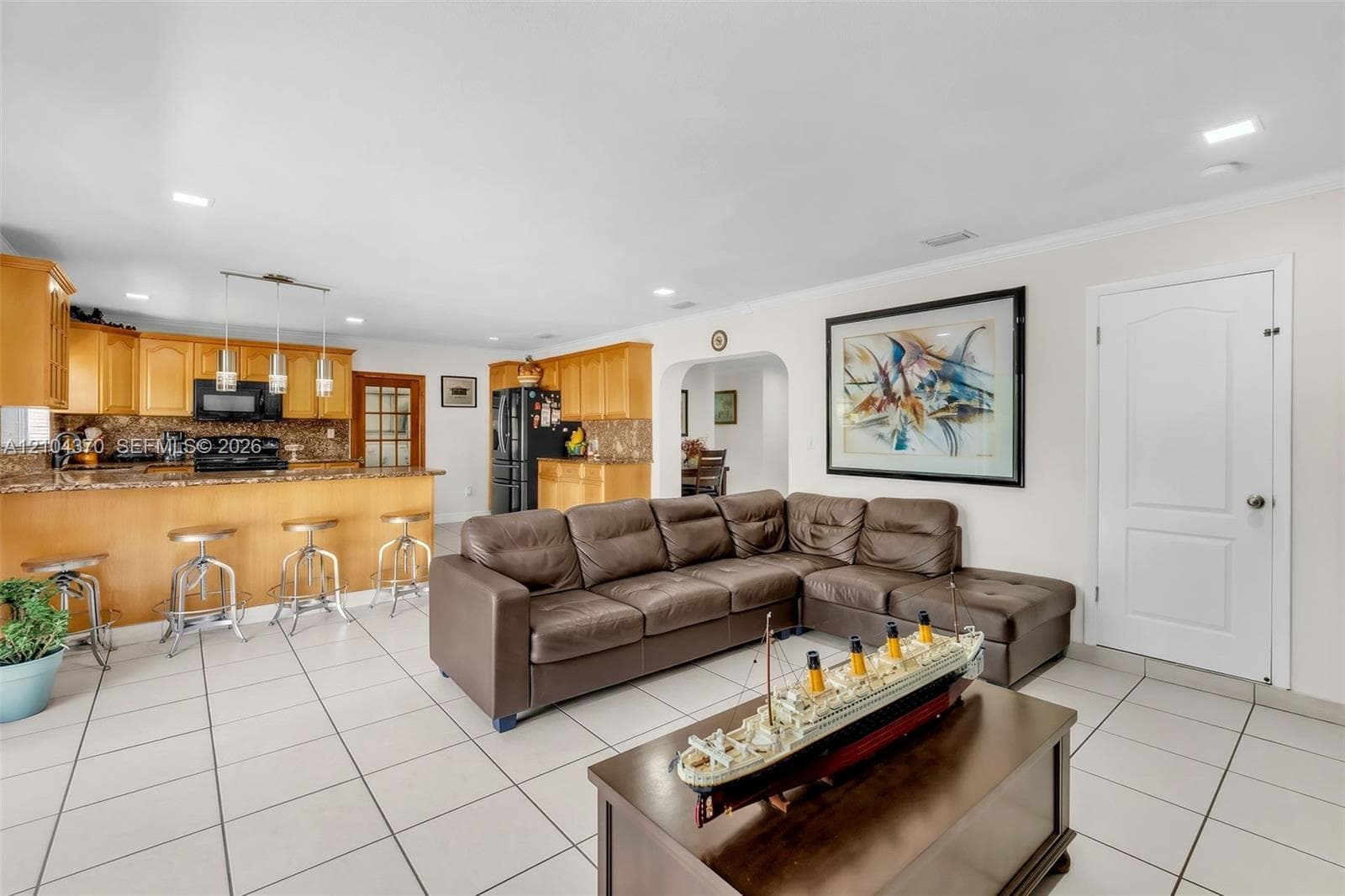 Spacious living area featuring large-format ceramic tile flooring, recessed lighting, crown molding, and a sliding glass door