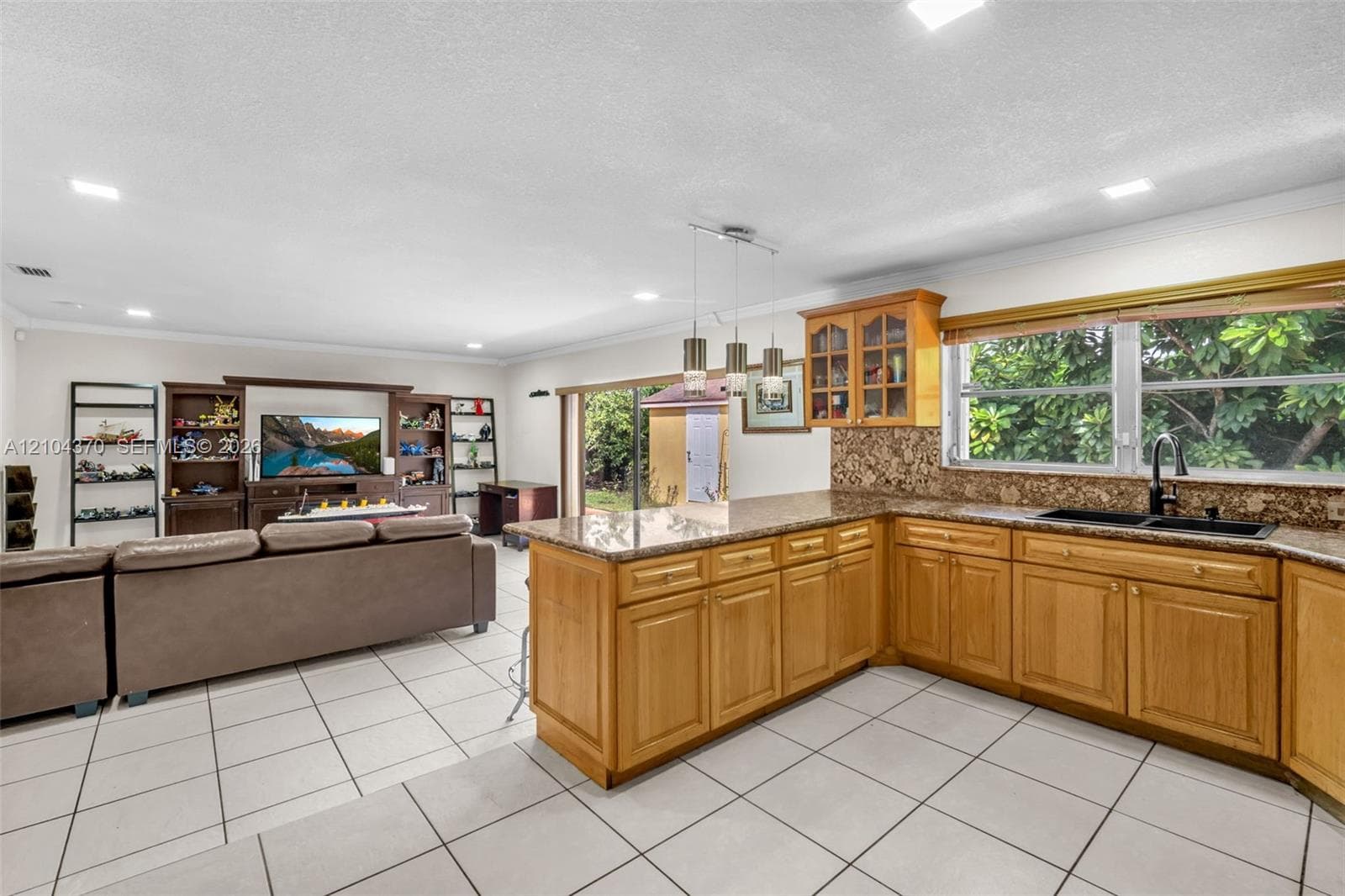 Kitchen featuring wood cabinetry, stone countertops, a breakfast bar, ceramic tile flooring, and triple pendant lighting