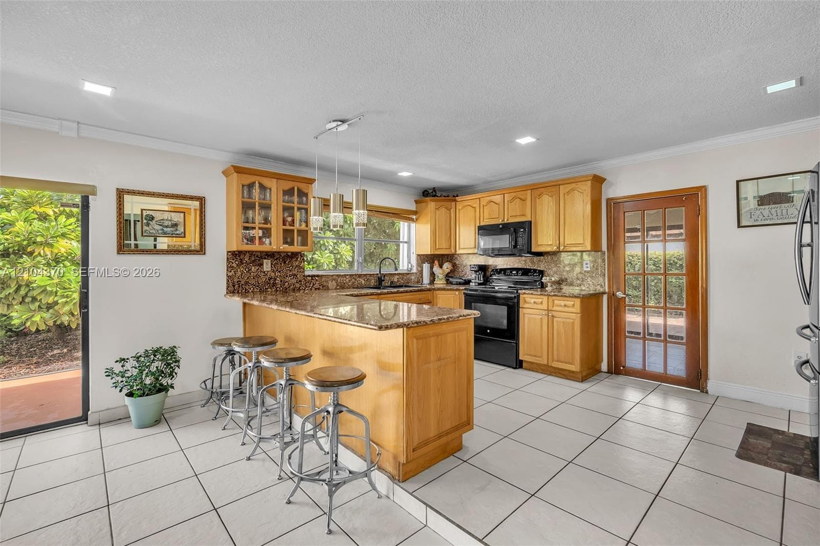 Open-concept living space featuring wood-finish cabinetry, a breakfast bar, recessed lighting, tile flooring, and sliding glass doors