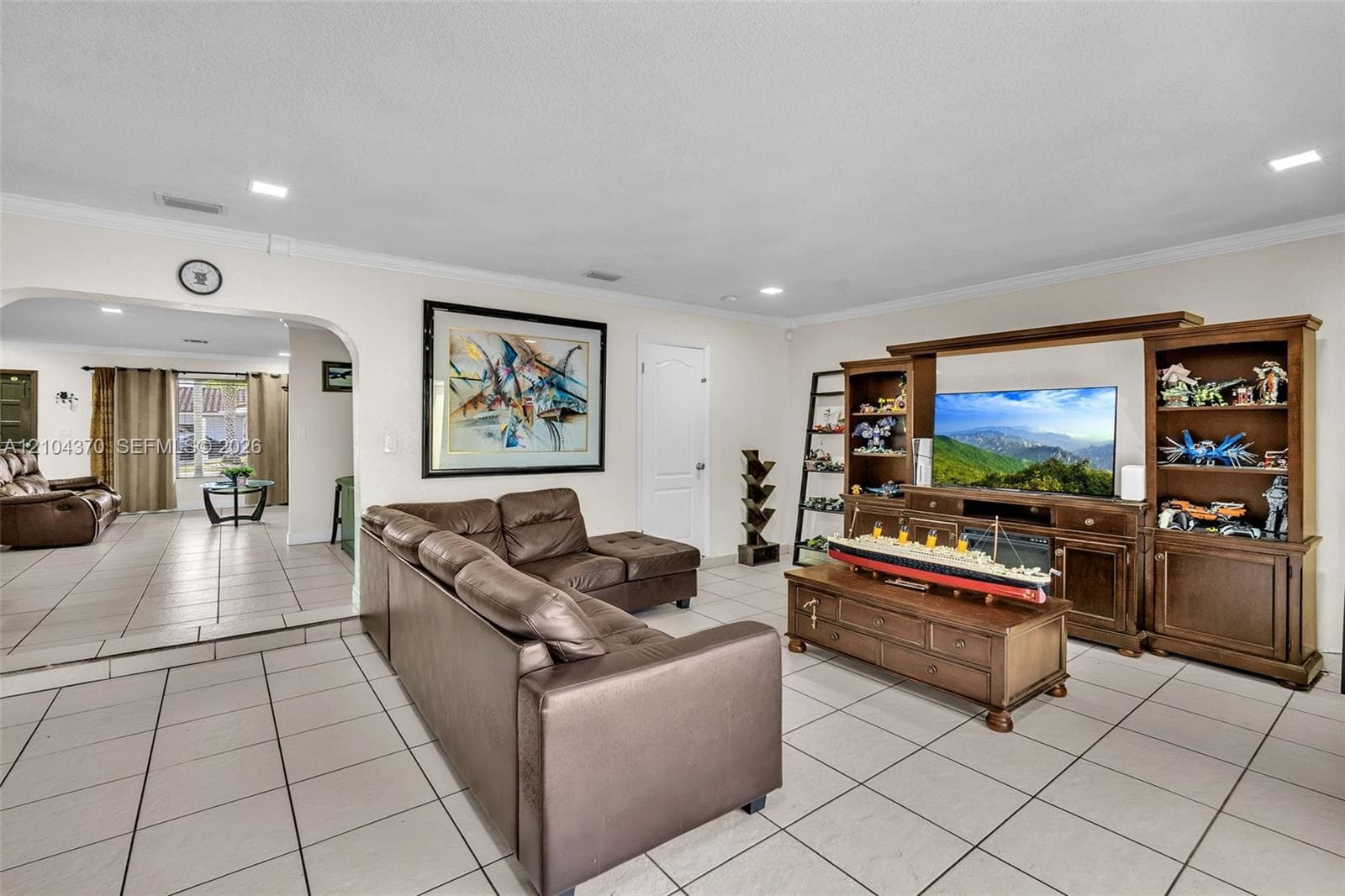 Dining area featuring large-format tile flooring, built-in black cabinetry with glass-paneled display doors, recessed lighting, and an arched doorway