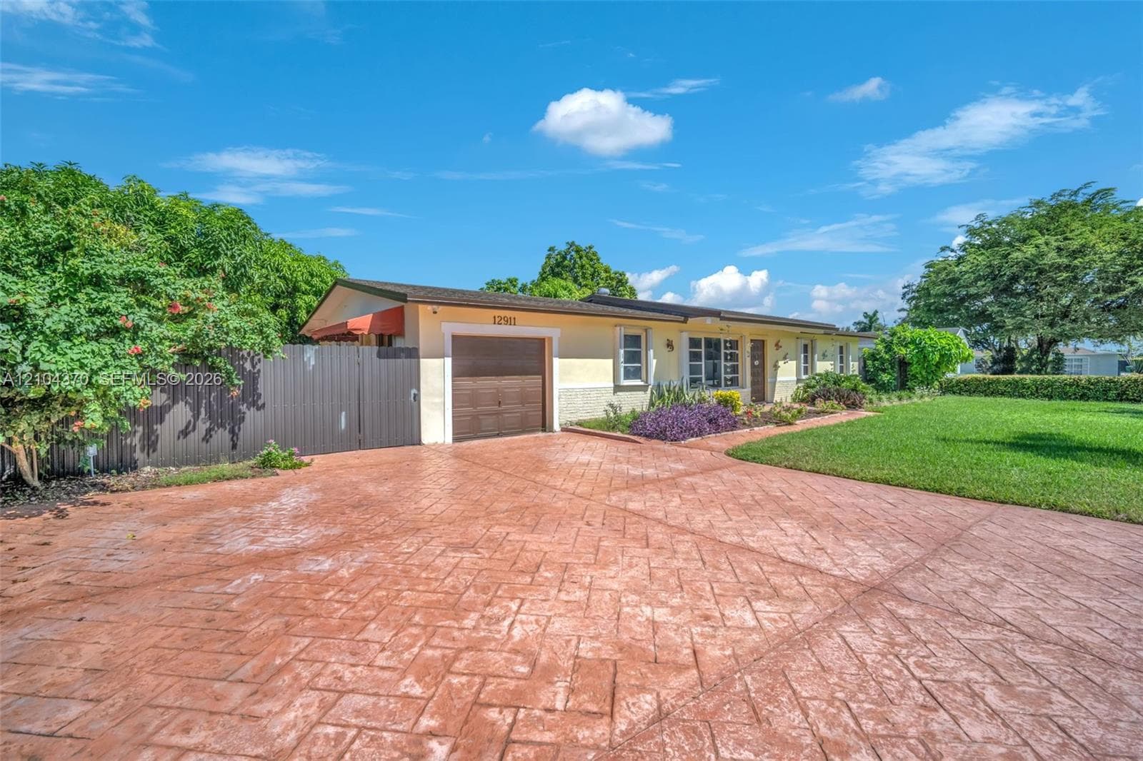 Aerial perspective of a residential lot featuring a paved driveway, established landscaping with mature palm trees, and a detached storage structure