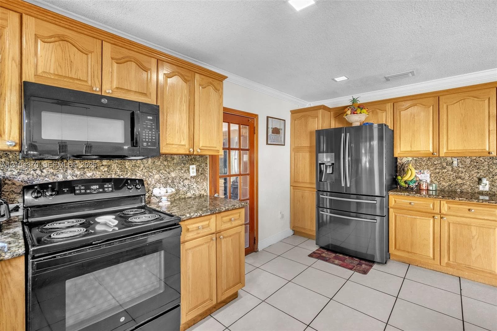 Kitchen featuring stone-finish countertops, warm-toned wood cabinetry with glass-front display accents, a double-basin undermount sink with a high-arc faucet, and modern cylindrical pendant lighting