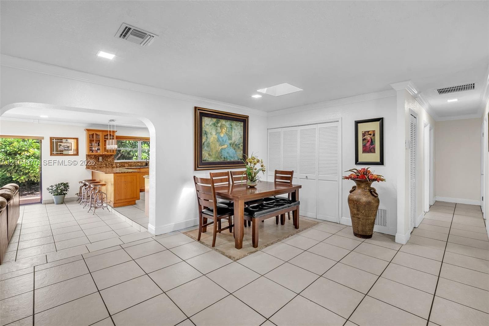 Open-concept interior featuring neutral ceramic tile flooring, recessed lighting, crown molding, and a distinctive arched doorway