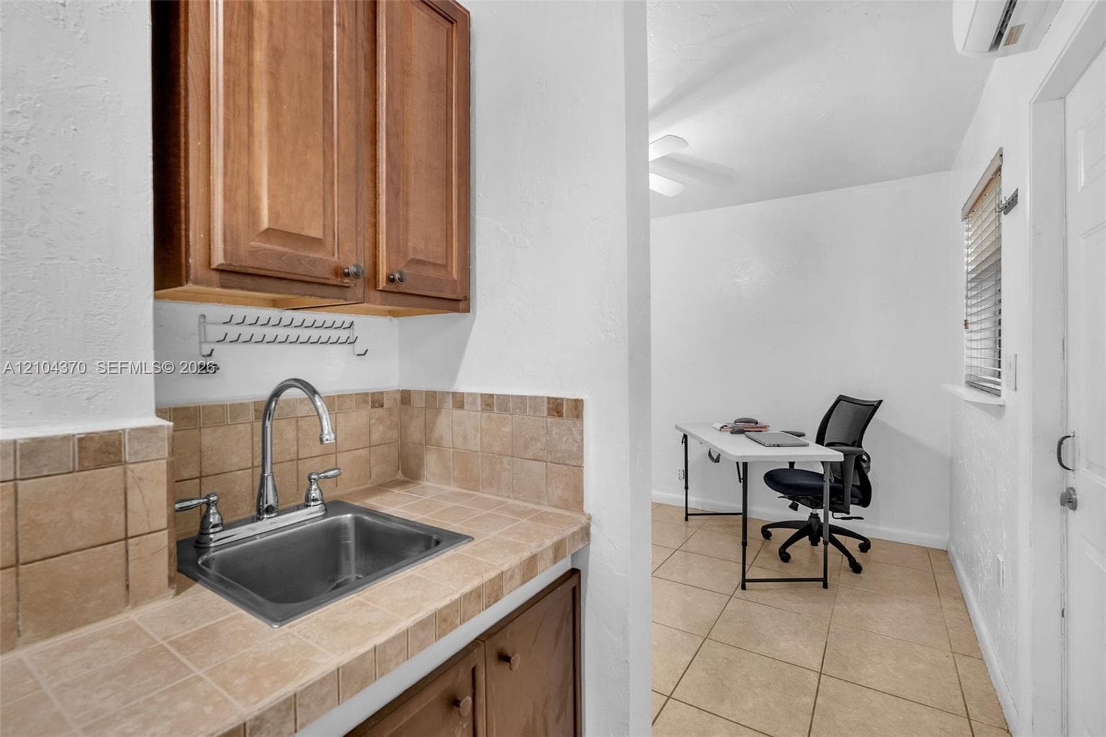 Room interior featuring neutral tile flooring, white walls, louvered-style closet doors, and a ceiling fan with integrated lighting