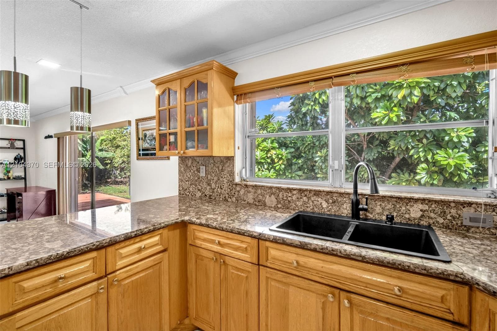 Kitchen featuring honey-toned wood cabinetry, stone countertops, tiled flooring, a multi-light pendant fixture, and a glass-paneled exterior door