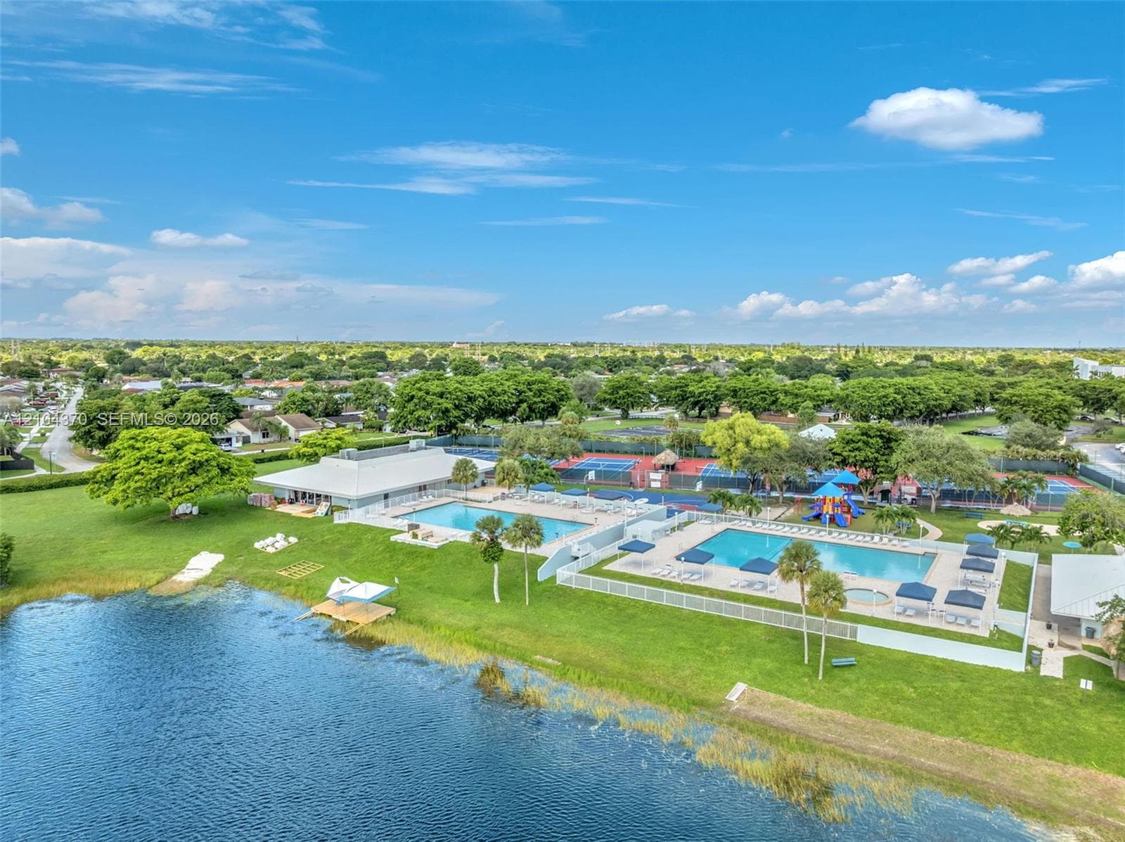 Community recreation area featuring dual outdoor swimming pools, multi-surface tennis courts, a playground, and waterfront access