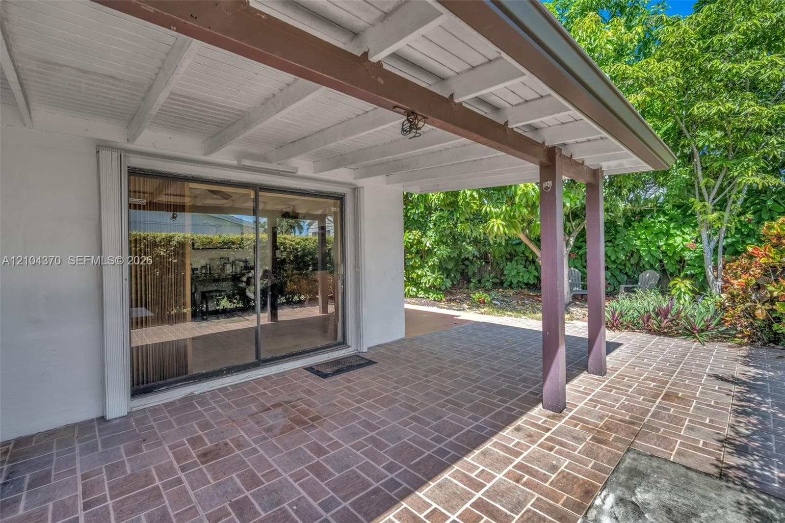 Covered patio featuring paver flooring, painted exposed-beam ceiling, and sliding glass door access