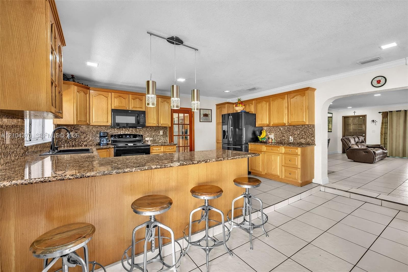 Open concept space featuring light-toned cabinetry, a stone-surfaced breakfast bar, recessed lighting, and large-format neutral floor tiling