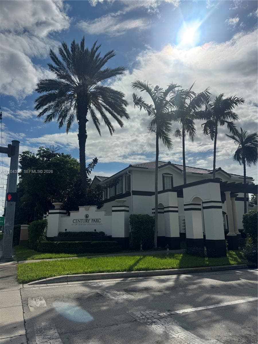 Gated community entrance featuring stucco masonry walls with decorative pillars, pergola architecture, and mature palm landscaping