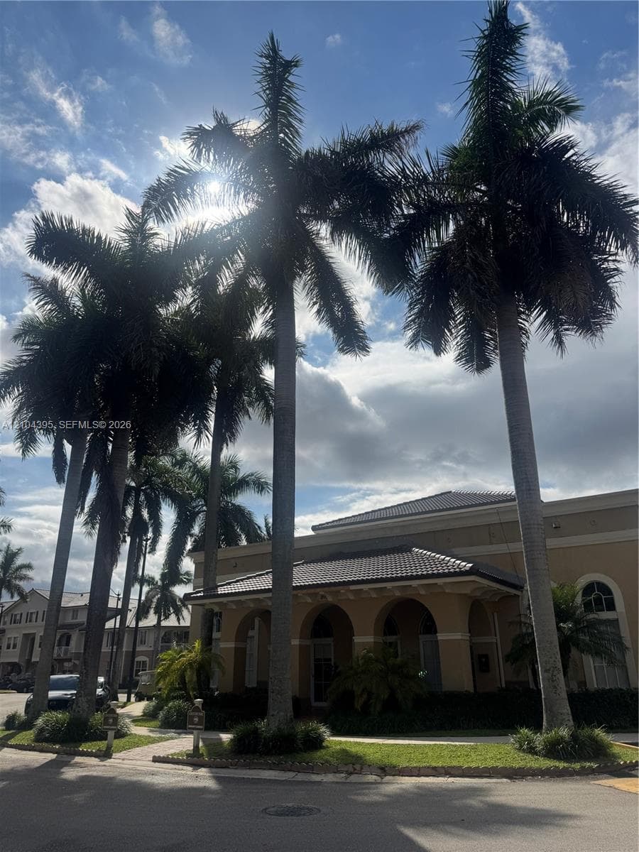 Exterior facade featuring arched entryways, tile roof, and mature palm trees