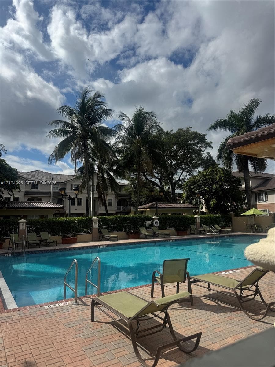 Swimming pool with brick-paver decking, metal entry rails, and mature palm trees
