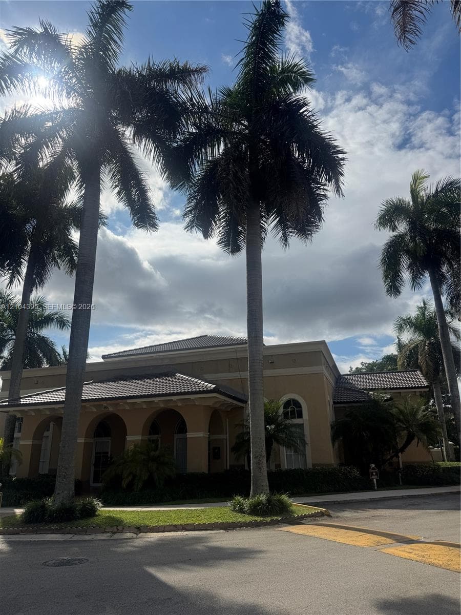 Exterior facade featuring a hipped roof, arched entryway, stucco-style siding, and mature palm trees