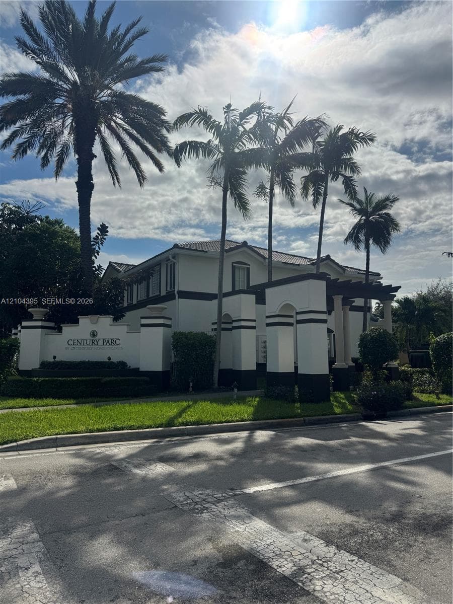 Stucco exterior featuring architectural columns, a covered entryway, and mature palm trees
