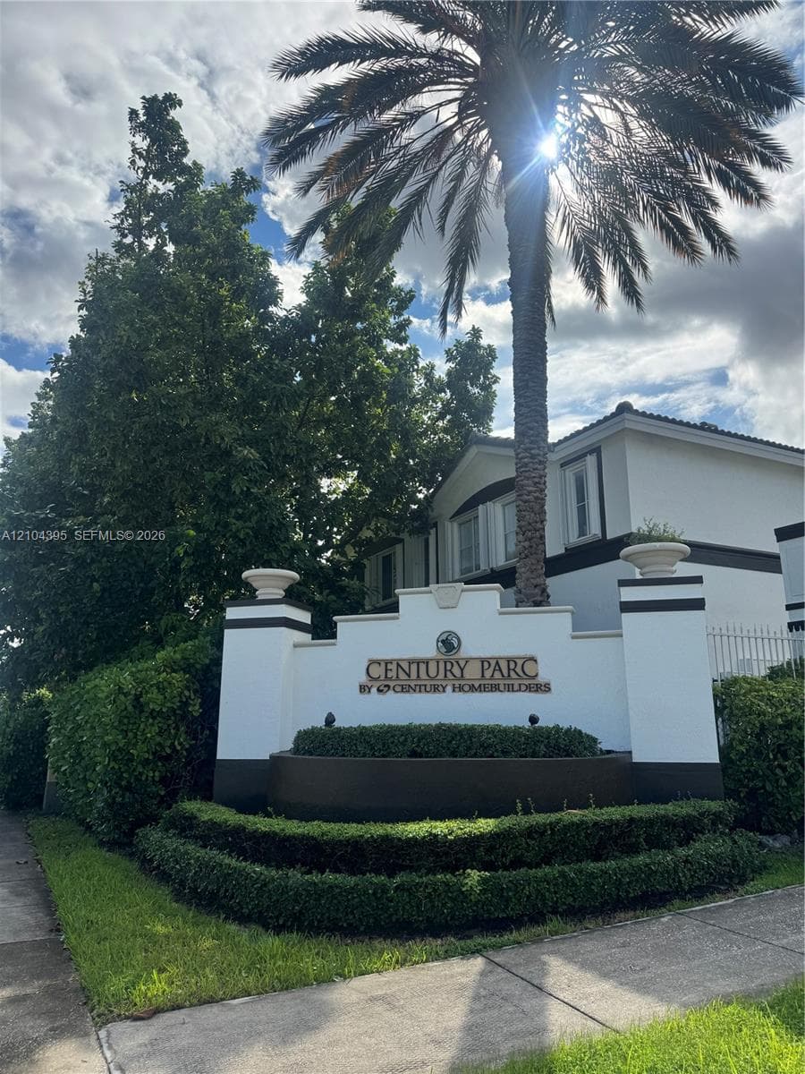 Community entrance sign featuring a masonry monument with decorative urns, manicured shrubbery, and mature palm tree landscaping