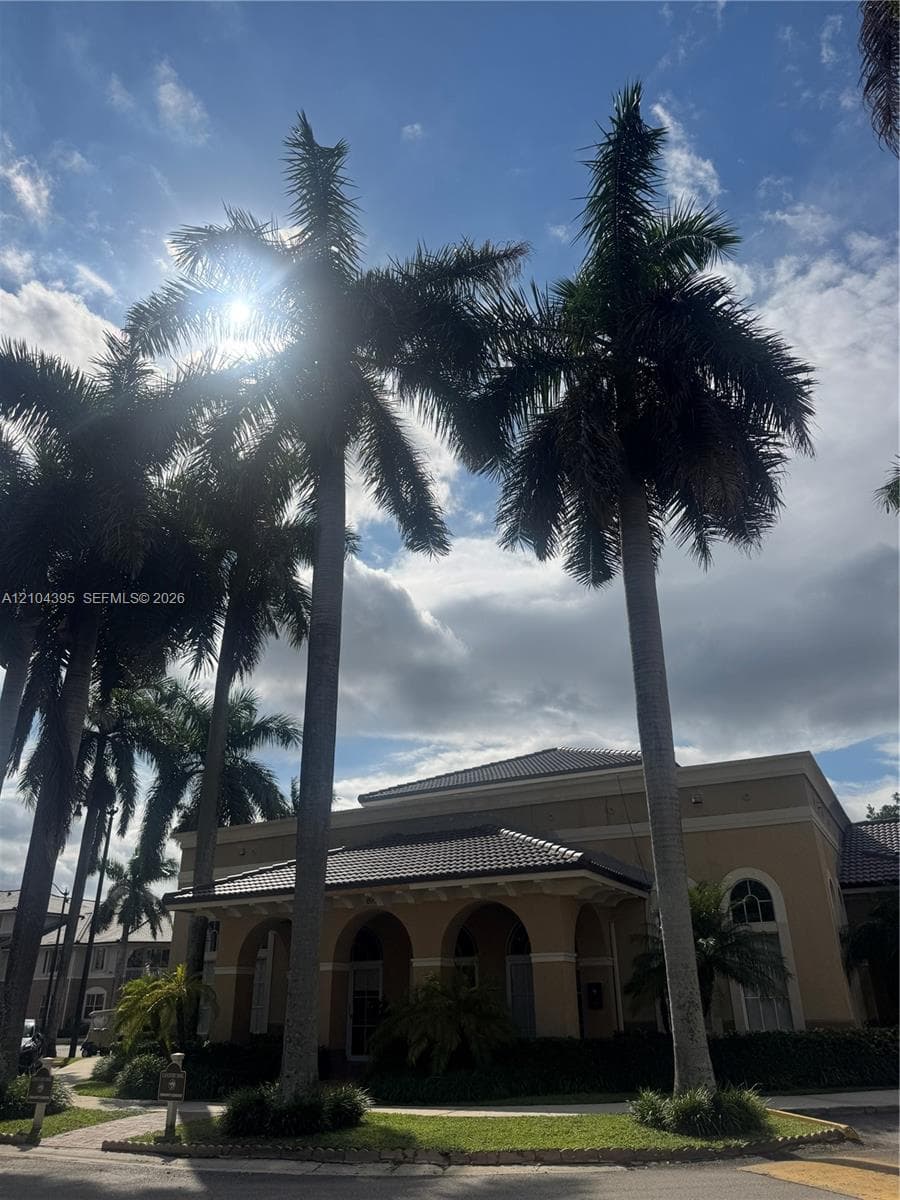 Stucco exterior with arched entryways and a tiled roof, accented by established palm trees and manicured landscaping
