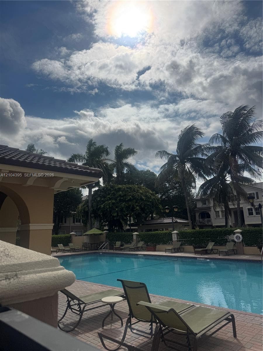 Swimming pool with a brick-paver deck, arched architectural details, and mature palm trees