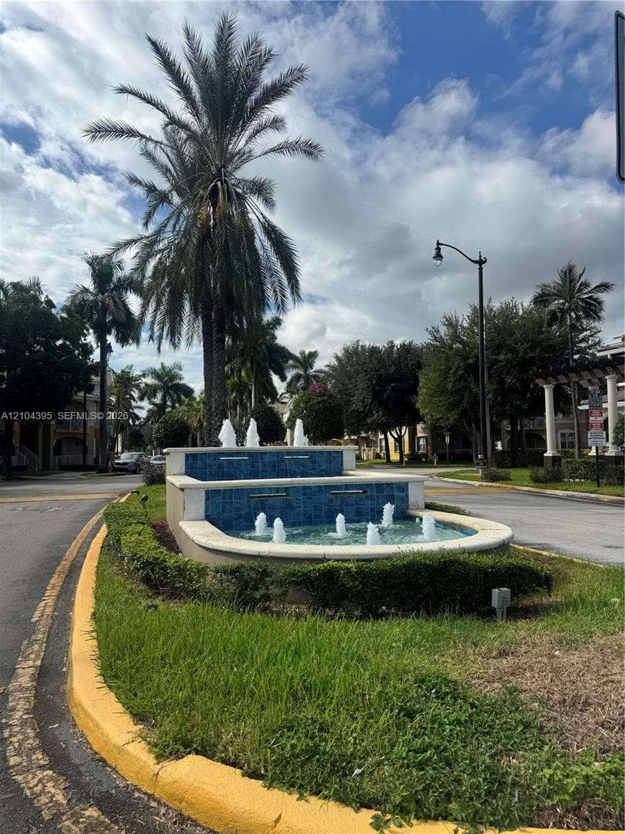 Tiered stone fountain featuring blue tile accents, multiple water jets, and a manicured landscape island with mature palm trees