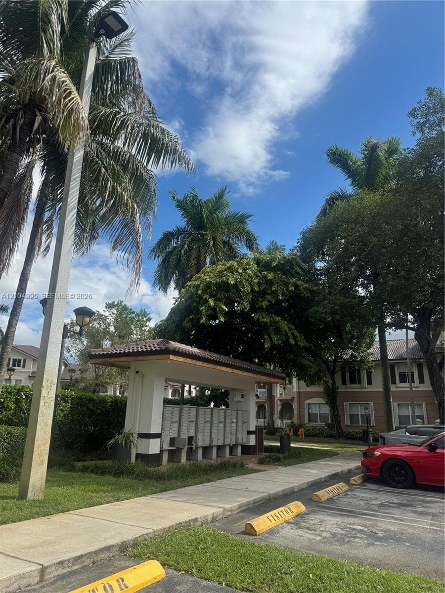 Covered mail kiosk structure featuring integrated lighting and paved access, surrounded by mature palm trees and landscaped grounds