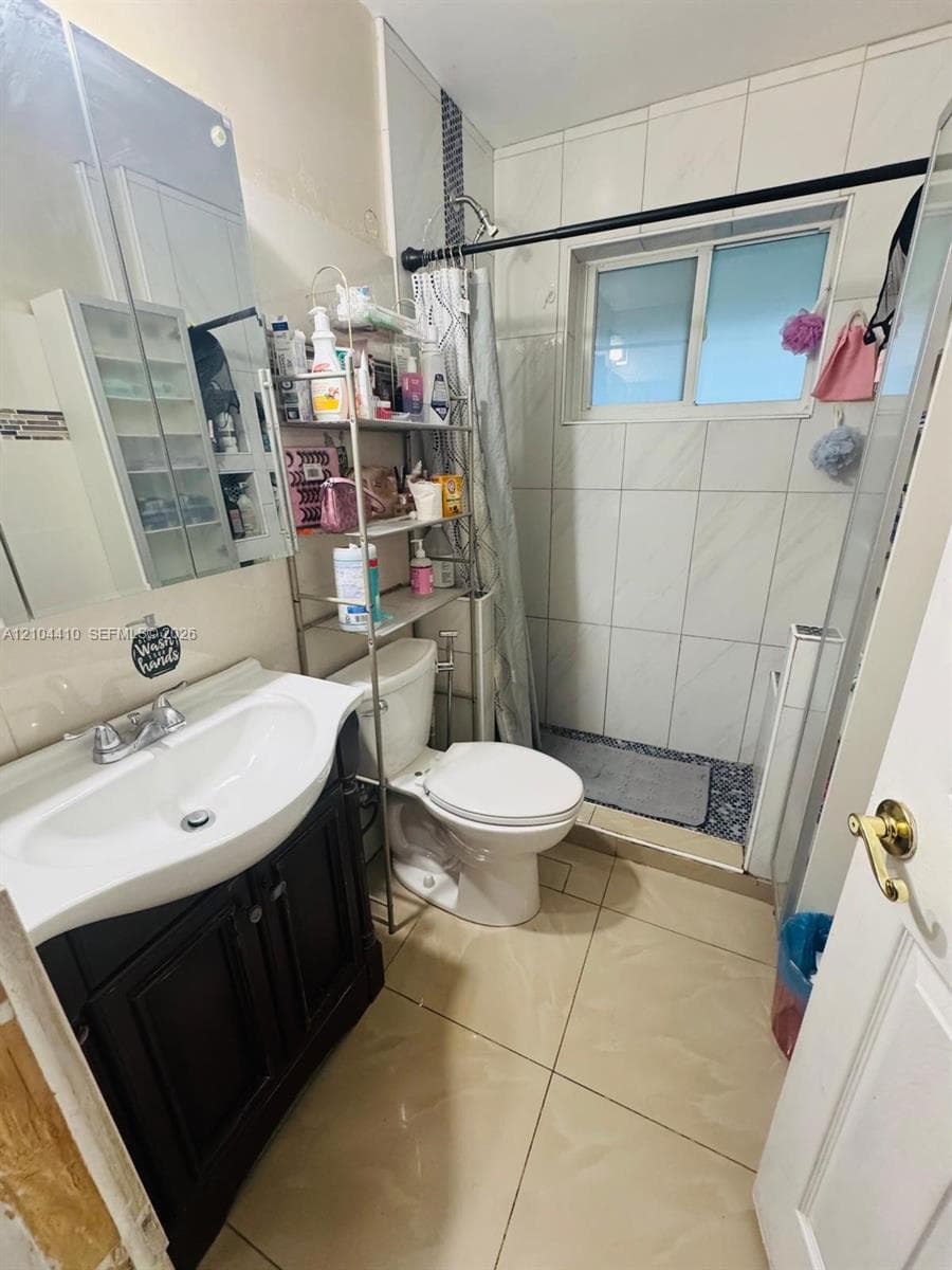 Bathroom featuring a dark-finish vanity with an integrated basin, large-format tile flooring, wall-tiled shower enclosure, and mirrored medicine cabinet