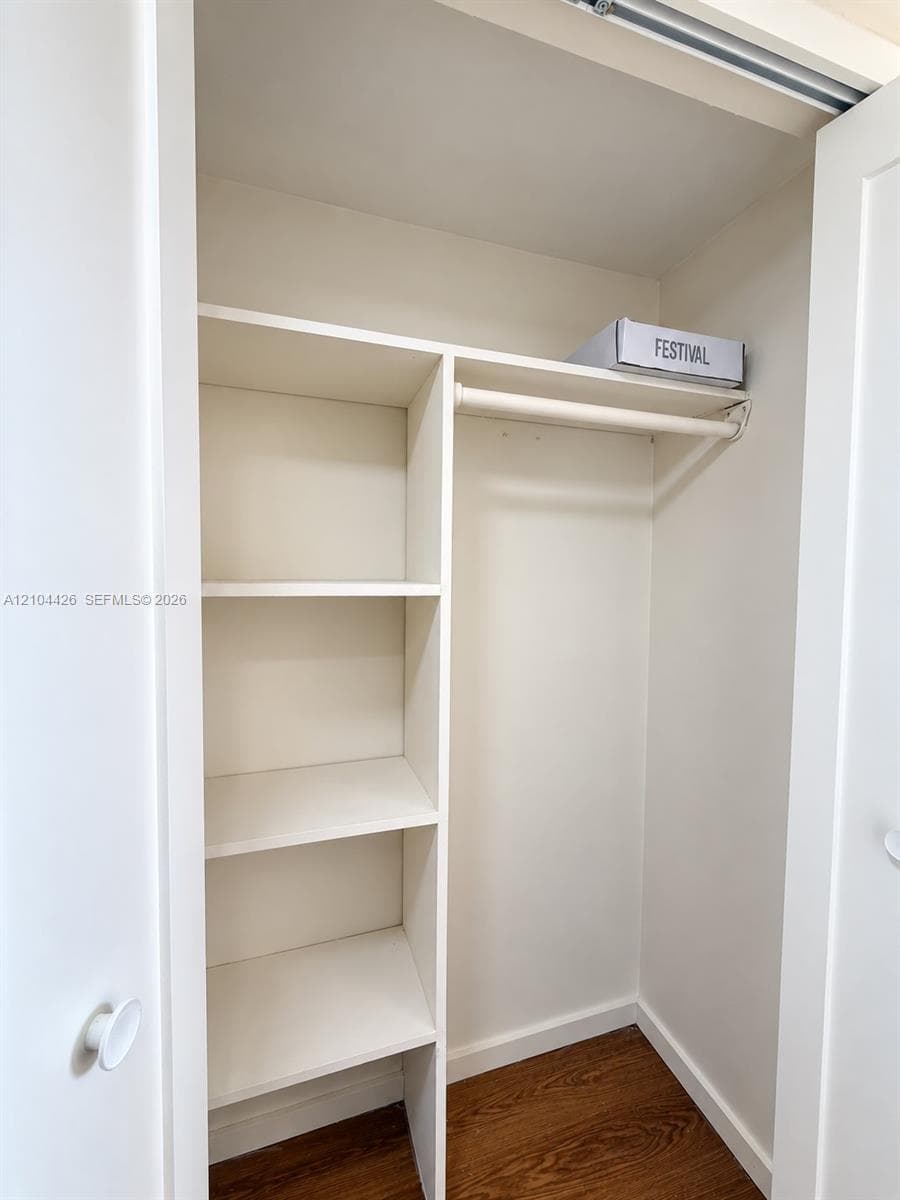 Built-in storage closet featuring white shelving units, a hanging rod, and wood-finish flooring