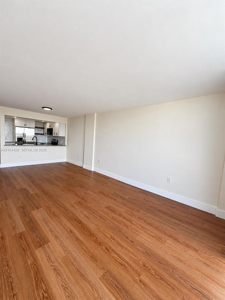 Open living area featuring wood-finish flooring, a pass-through opening to the kitchen, white cabinetry, a neutral countertop, and a dark-finish faucet