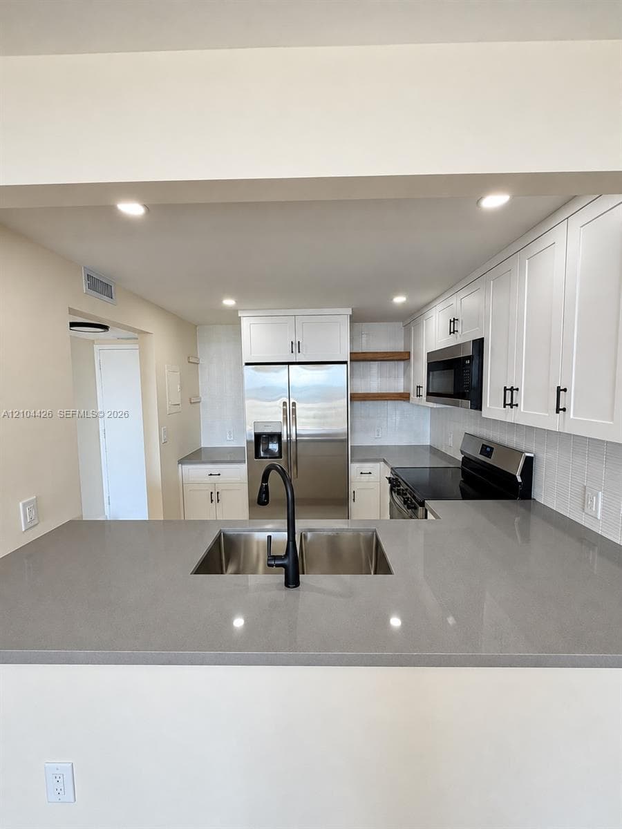 Kitchen featuring quartz countertops, white shaker-style cabinetry, stainless steel appliances, open wood shelving, and a matte black gooseneck faucet