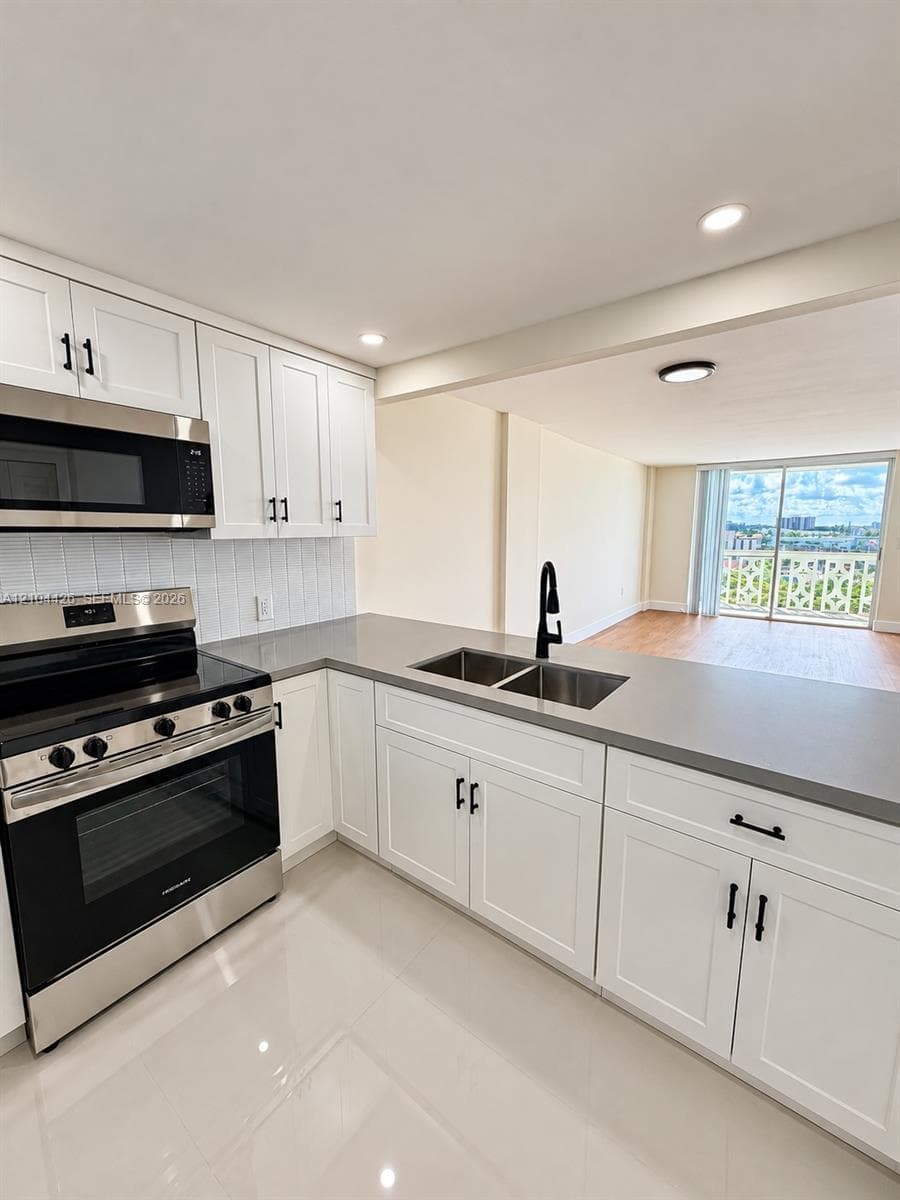 Kitchen featuring white shaker-style cabinetry, quartz countertops, stainless steel appliances, a double-basin undermount sink with a matte black faucet, and polished tile flooring