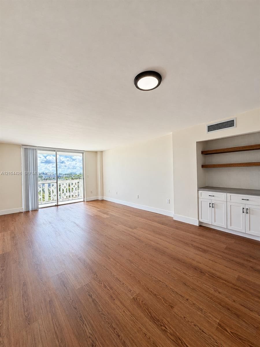 Open-concept room featuring wood-finish flooring, white built-in cabinetry with stone-finish countertops, floating shelving, a flush-mount light fixture, and floor-to-ceiling glass sliding doors