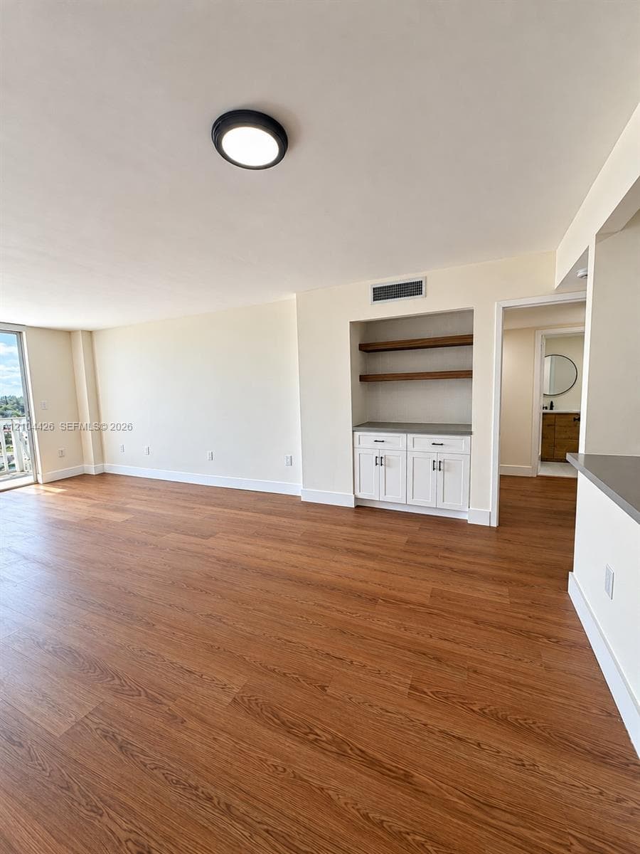 Wood-finish flooring, built-in cabinetry with stone-surface countertop, and floating wood shelving