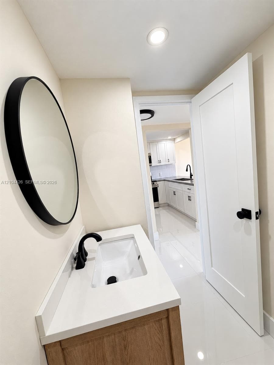 Wood-finish vanity cabinet with a white countertop, rectangular integrated sink, matte black faucet, and circular wall-mounted mirror