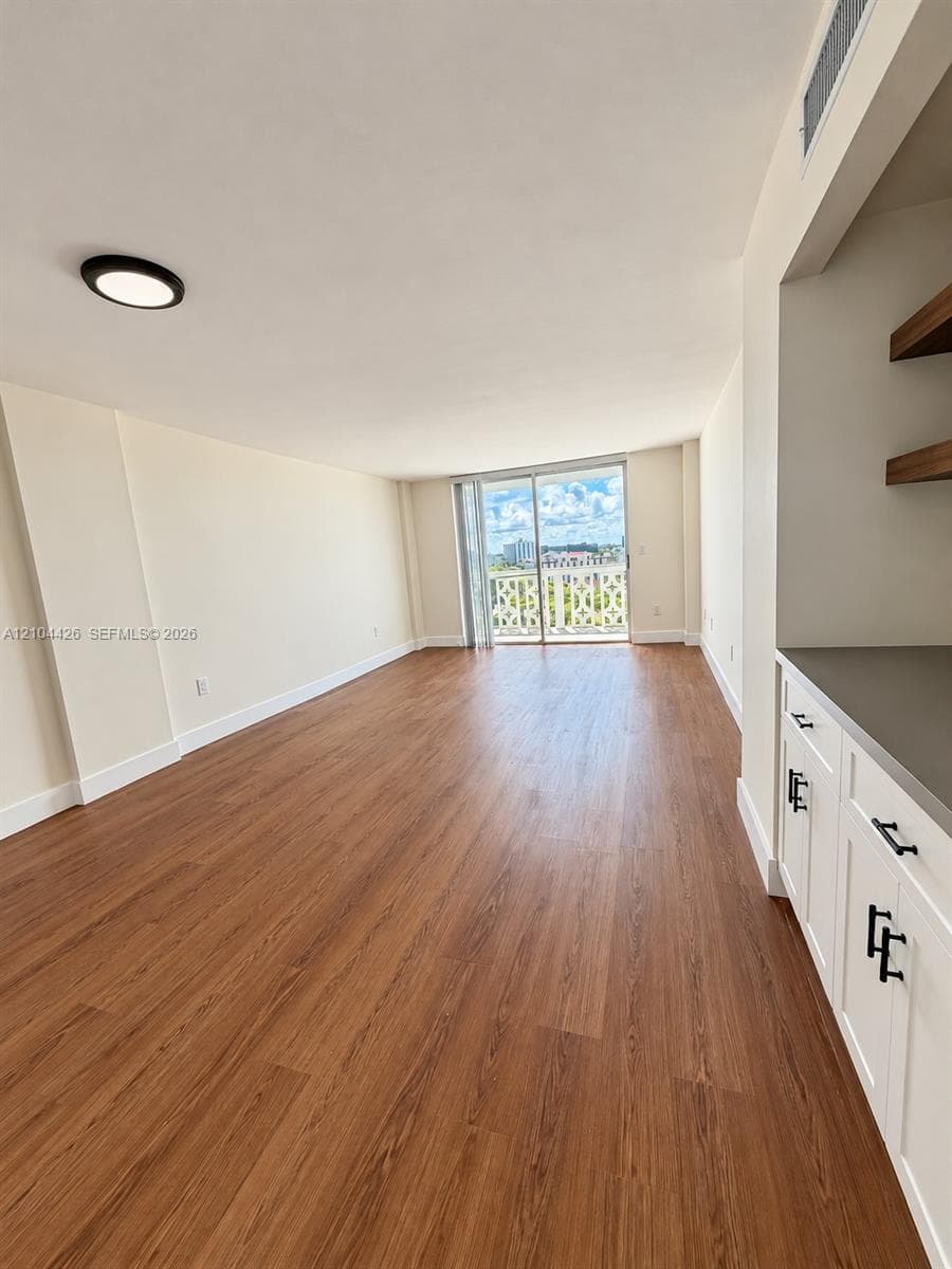 Open-concept room featuring wood-finish flooring, white built-in cabinetry with matte black hardware, stone-surface countertop, natural wood shelving, and floor-to-ceiling glass sliding doors